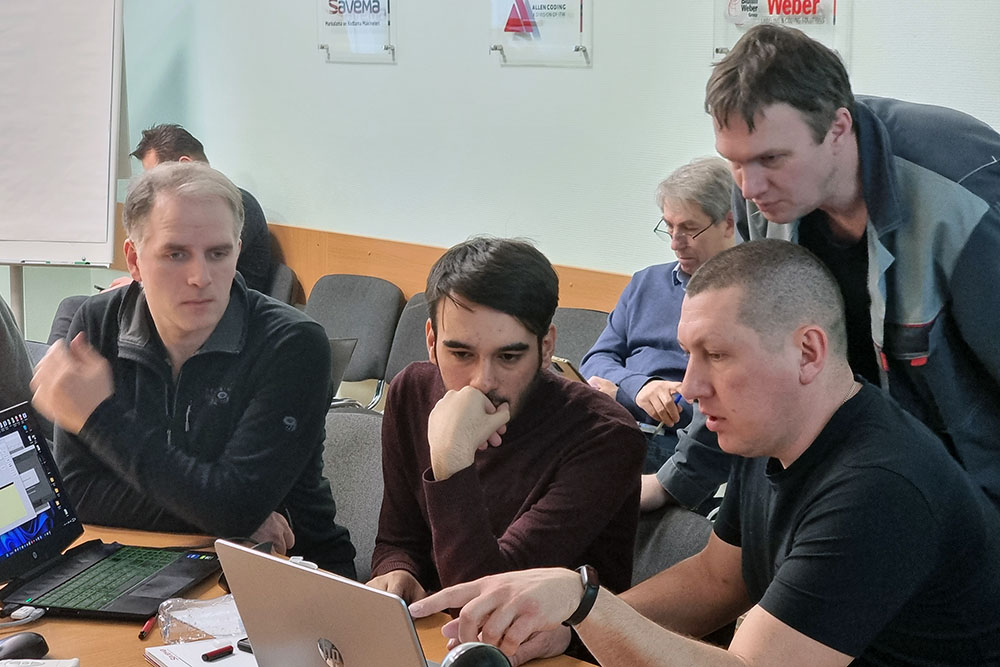 Группа мужчин сосредоточенно работает вокруг ноутбука в офисной обстановке Форинтека